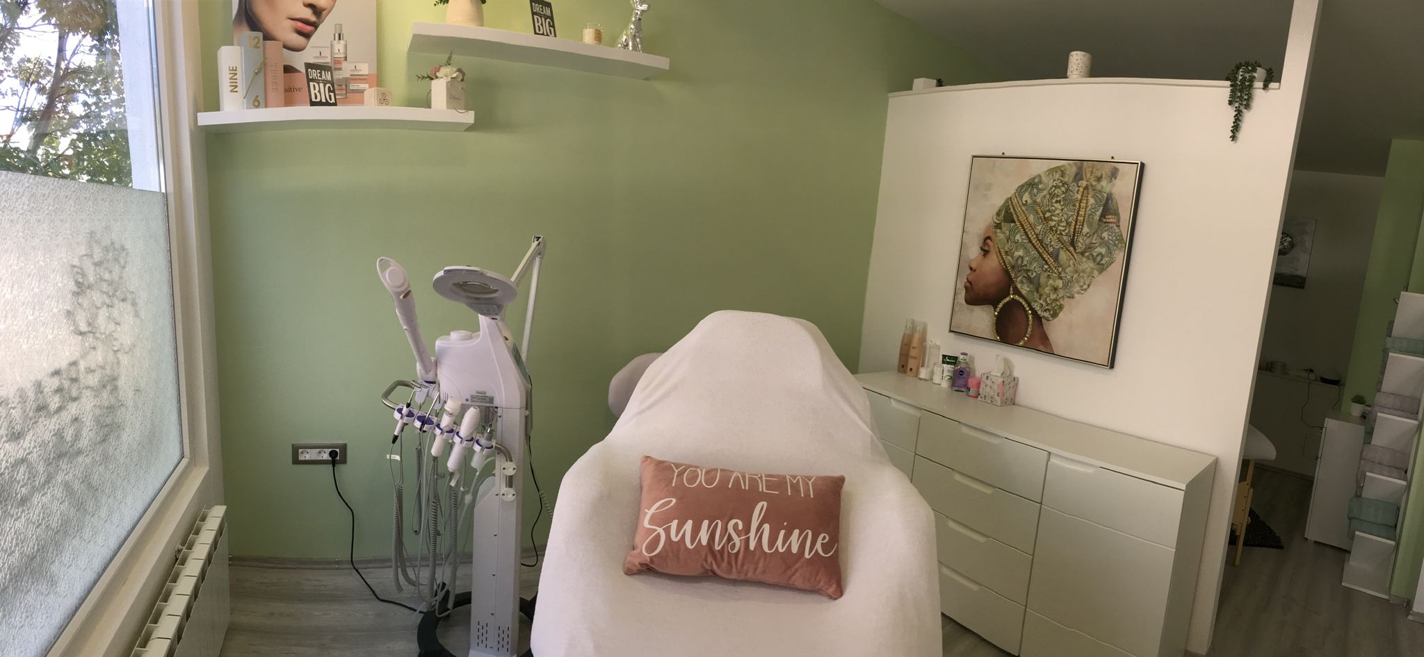 Prostor kozmetičkog salona nježno zelenih zidova i sa stolicom na sredini koja služi za tretmane lica i jastukom na kojem piše 'You are my sunshine'